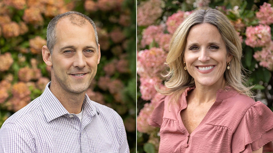 A smiling man with short gray hair in a short sleeve button-up short, with a background of orange flowers behind him, and a smiling woman with blonde hair in a coral blouse, with a background of pink flowers behind her.