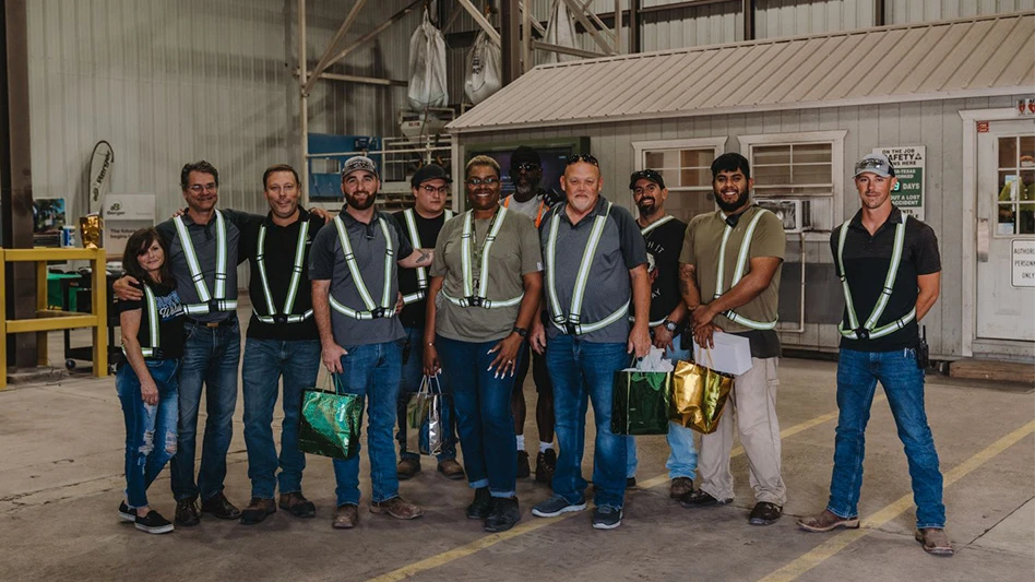 A group of 11 people smile and pose for a photo in a warehouse.