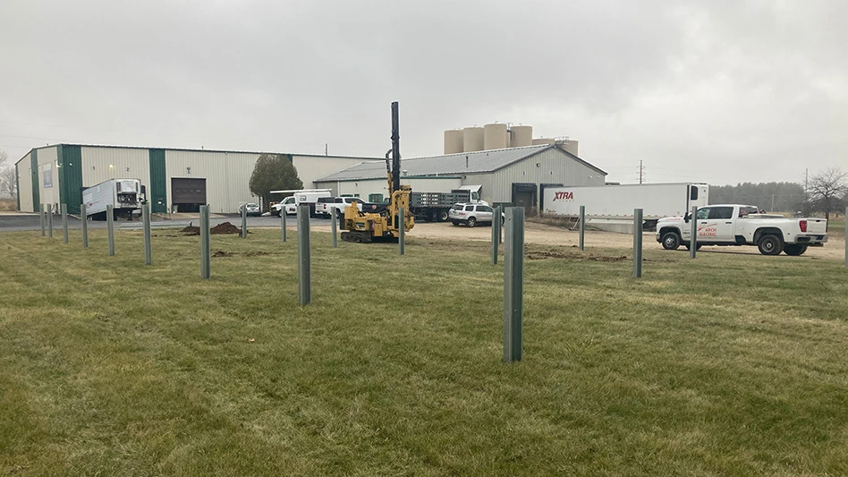 A large cream and green commercial building, with multiple vehicles parked around it and green grass in front of the building with gray posts coming out of the grass.