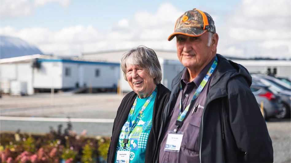 An older man and woman stand in the parking lot in front of a nursery facility.