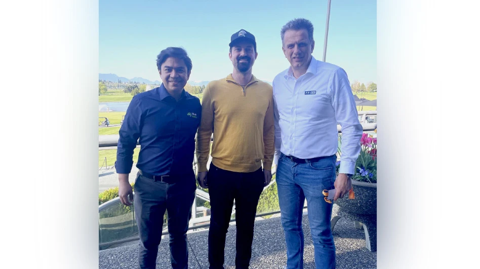 Three smiling men standing together in front of a landscape view.