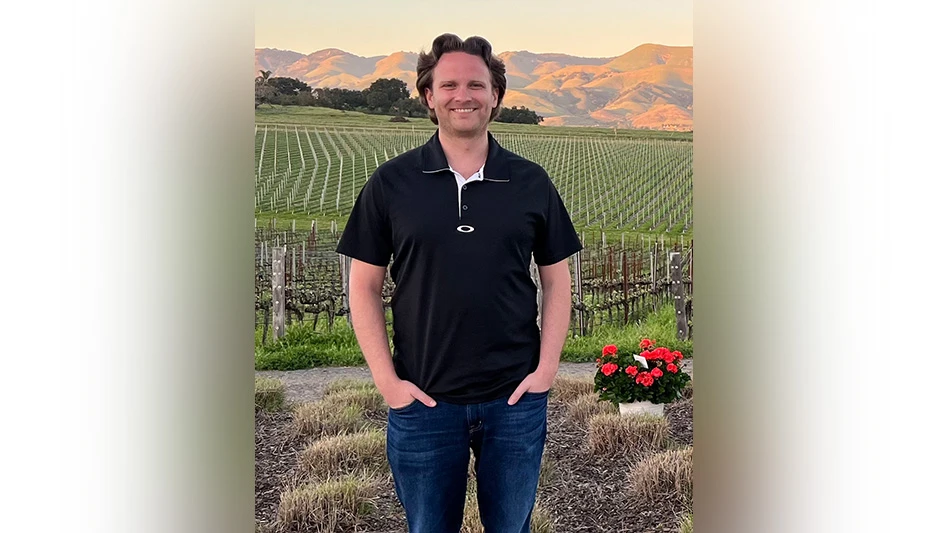 Man poses in front of vast green field and mountains.