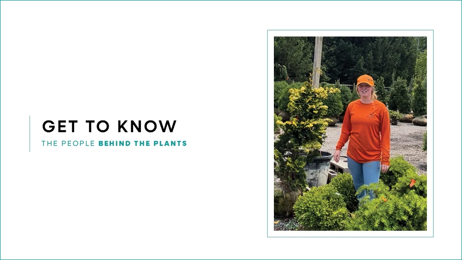 A women standing in a wholesale nursery surrounded by plants. She's wearing an orange t-short and hat.
