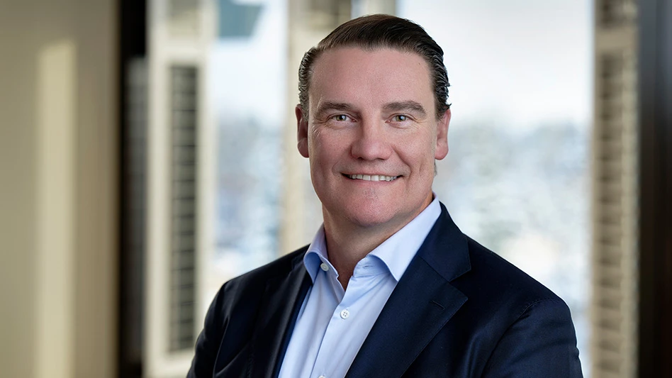 A headshot photo of a smiling man with short brown hair and wearing a navy blue suit jacket and light blue button-up shirt.