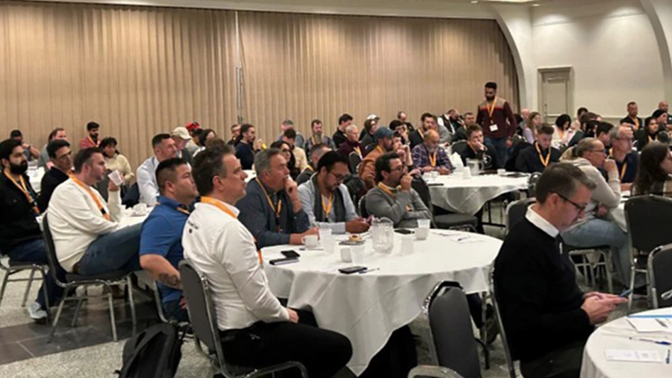 A crowd of people sit at circular white tables in an event hall.