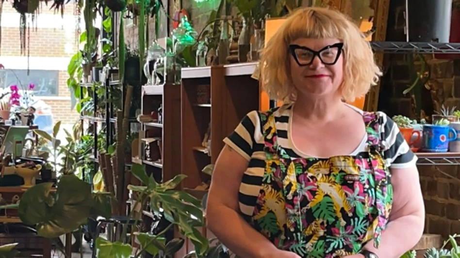 Amanda Thomsen standing in front of plants on wooden shelves.