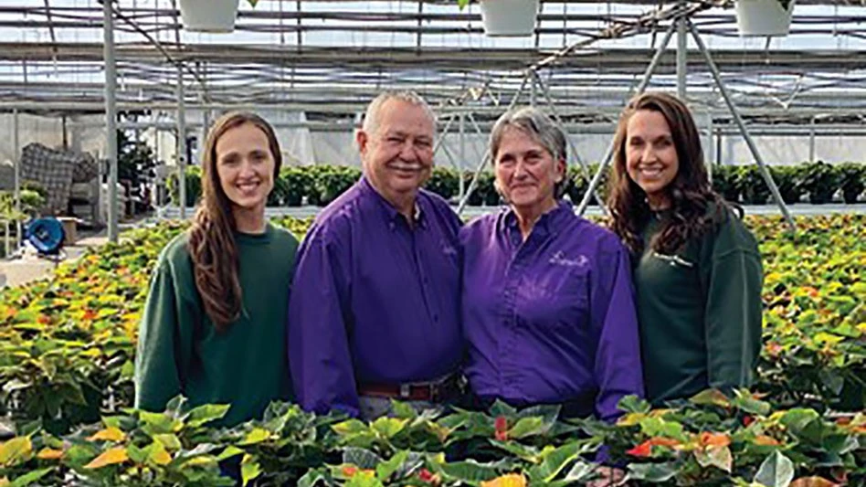 Four people stand together smiling at the camera standing among their plants.